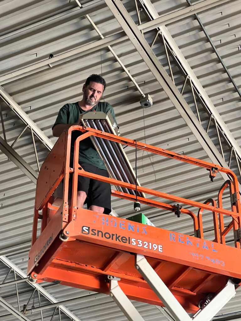 Commercial electrician installing LED High Bay Fixture in manufacturing facility.