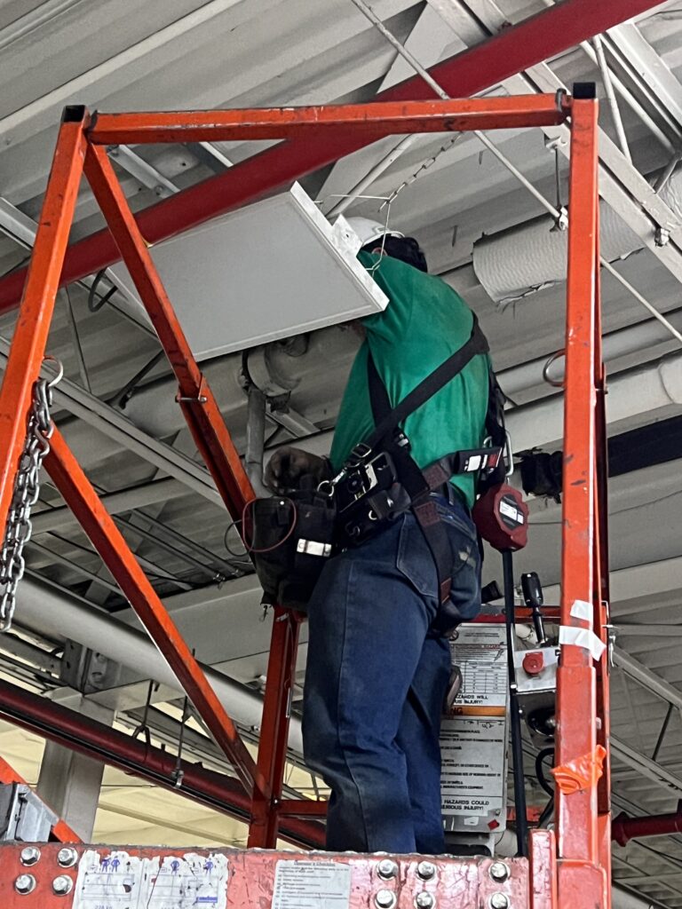 Commercial electrician installing LED High Bay Fixture in manufacturing facility.